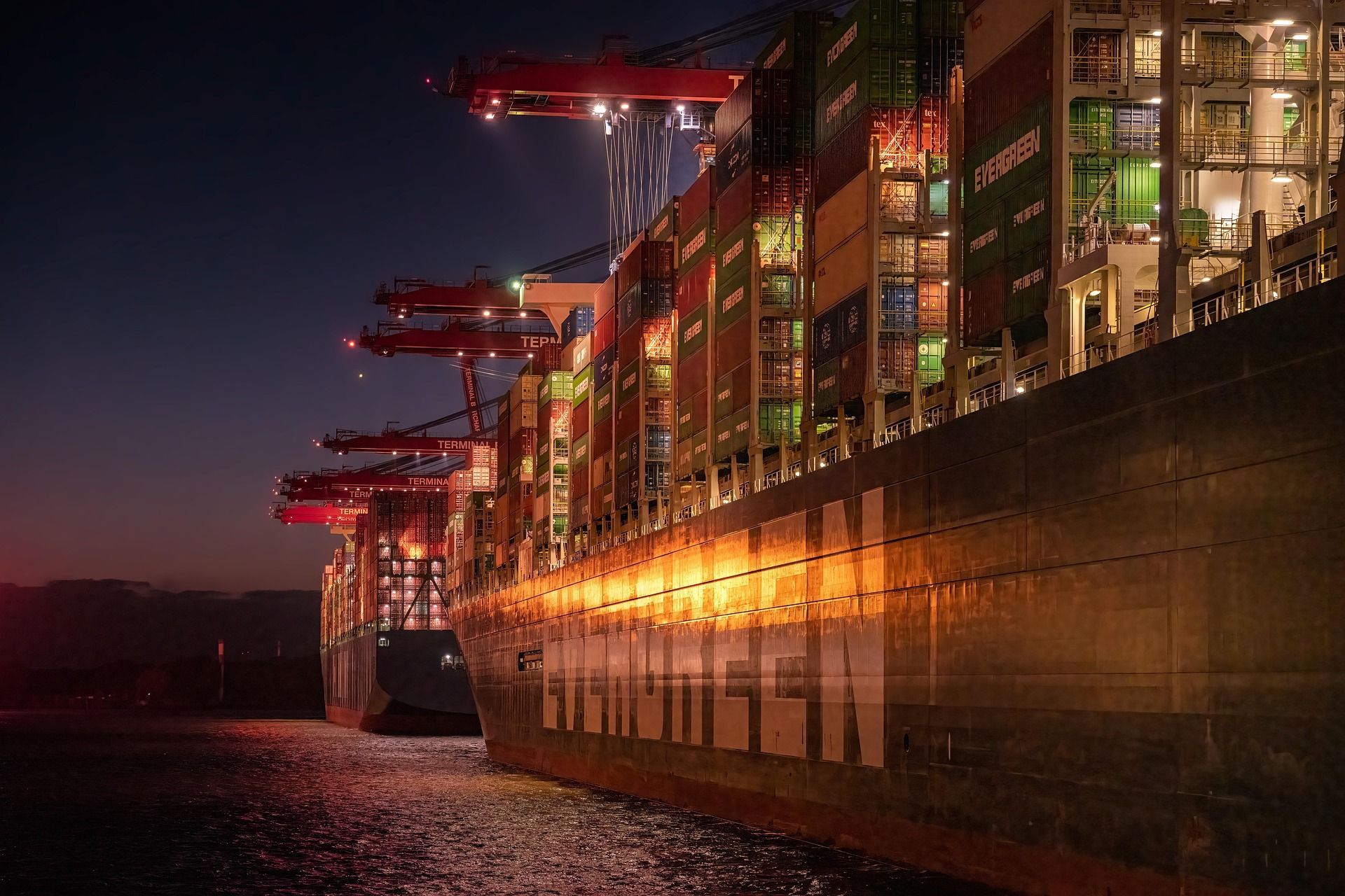 A container ship alongside under quay cranes at night